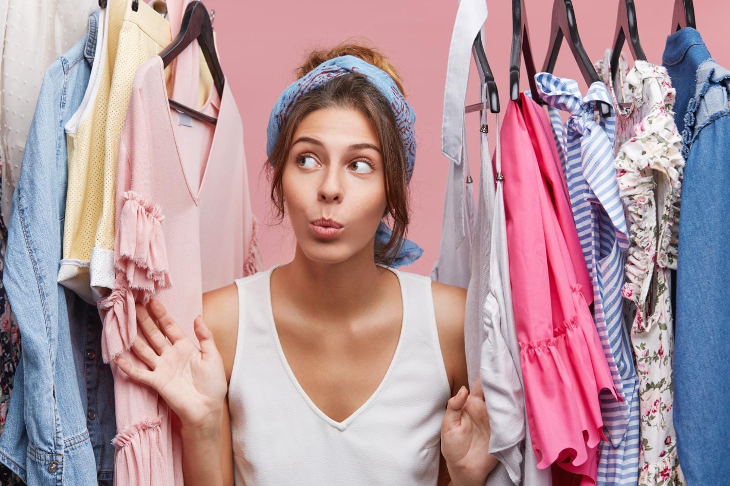attractive woman dressed casually looking with doubts aside while standing near hangers with clothes thinking what dress business meeting with companions woman fashion having many clothes loveisaname